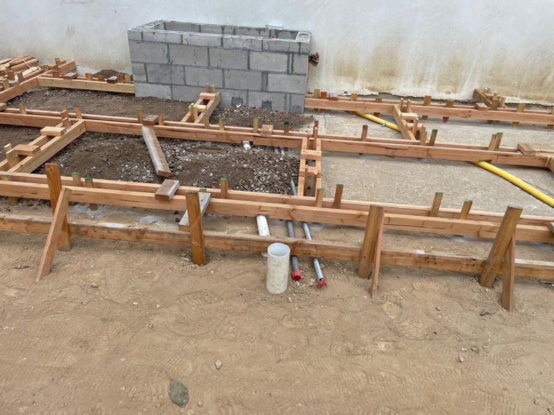 Wood forms staked on a compacted gravel base for a concrete patio beside a white plaster wall