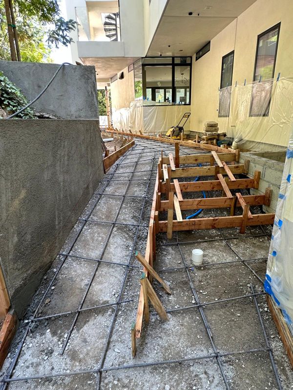 Side-yard walkway rebar on gravel with wood step forms beside a concrete wall