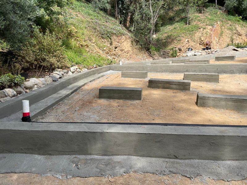 Newly poured retaining wall and planter curbs with a river-rock border on a hillside