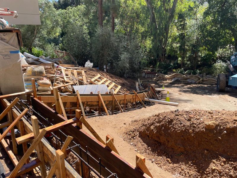 Curved wood forms with tied rebar cages for a retaining wall footing on a hillside
