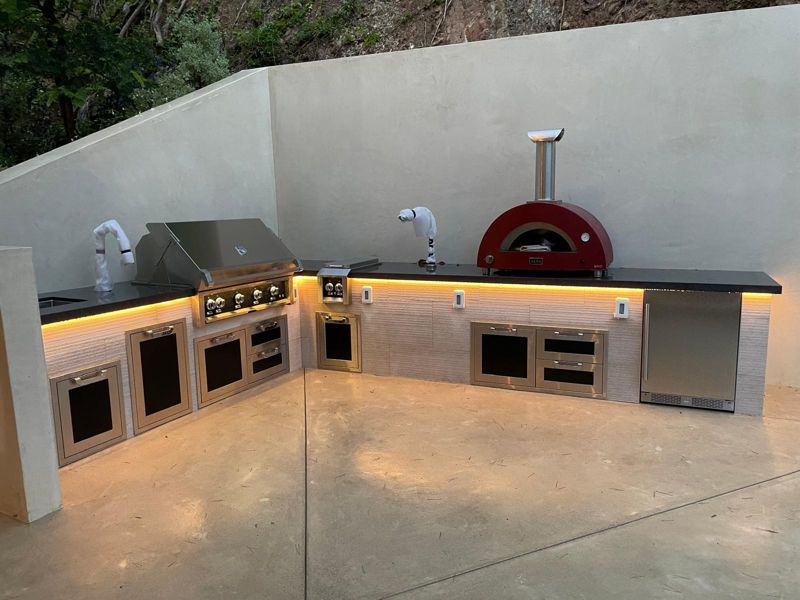 Front view of the finished outdoor kitchen with grill, side burner, pizza oven, stainless doors and fridge