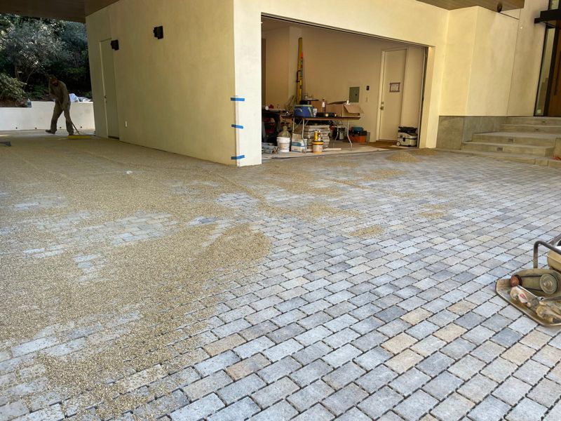 Joint sand being swept into a tumbled paver motor court in front of a garage