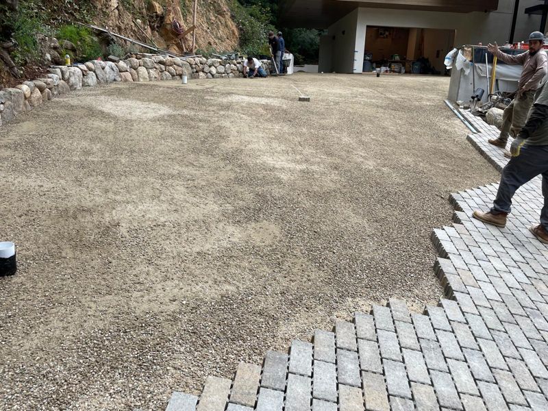 Pavers being laid over a compacted gravel and sand base toward a garage