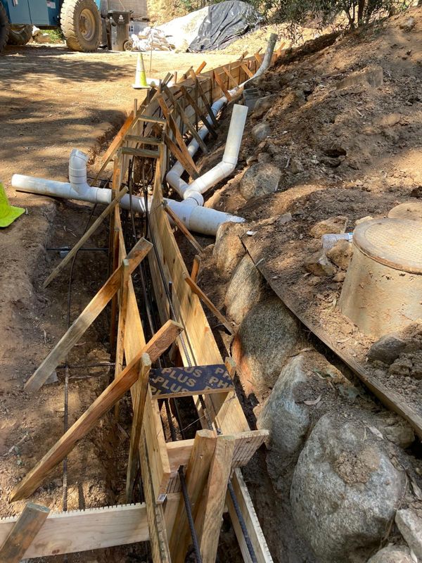Long wall form with vertical rebar and drain pipes along a cut hillside