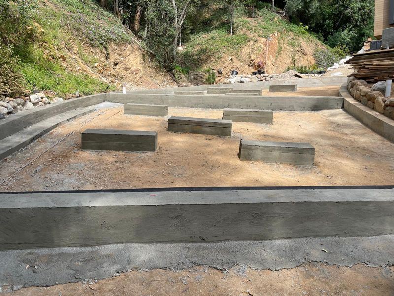 Newly poured and plastered concrete retaining walls and curbs enclosing a level pad on a hillside