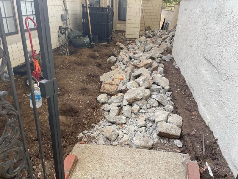 Side yard during demolition, with the old concrete path broken up and piled down the center