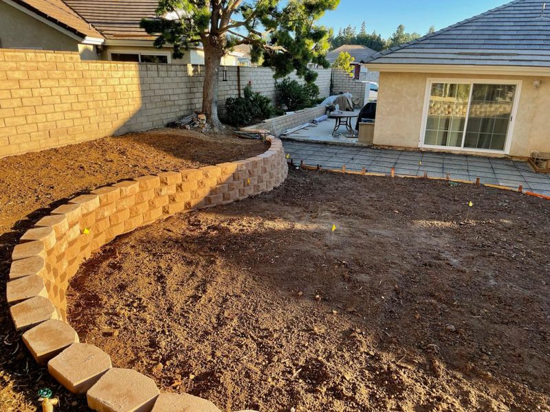 Newly built curved split-face block retaining wall around a graded backyard