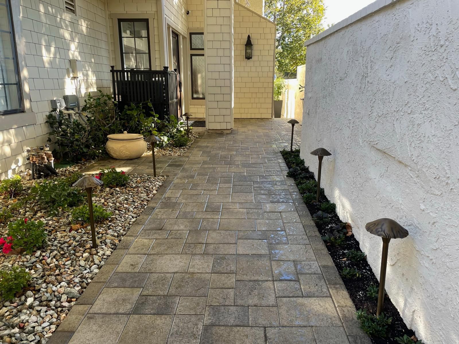 Paver walkway with path lights and a gravel planting bed between a shingle house and a stucco wall