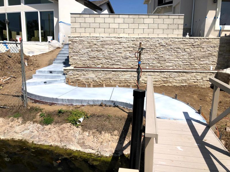 Freshly poured curved concrete walkway and steps along a stacked-stone wall at the lake edge