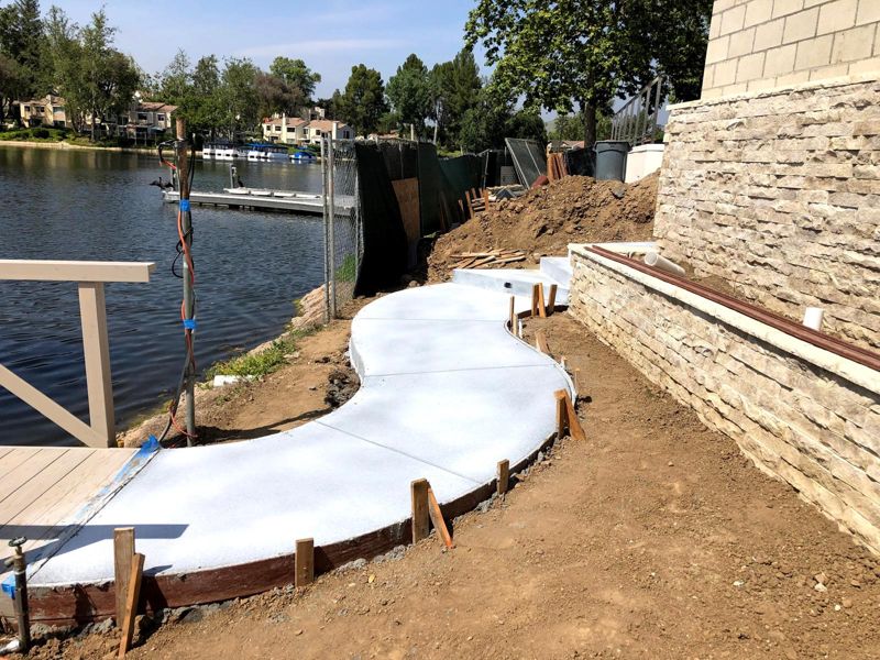 Curved concrete walkway still in wood forms along a stacked-stone retaining wall by the lake