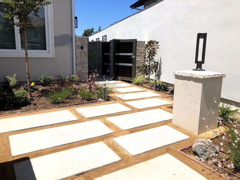Large concrete pavers set in decomposed granite in a side yard, with new planting beds