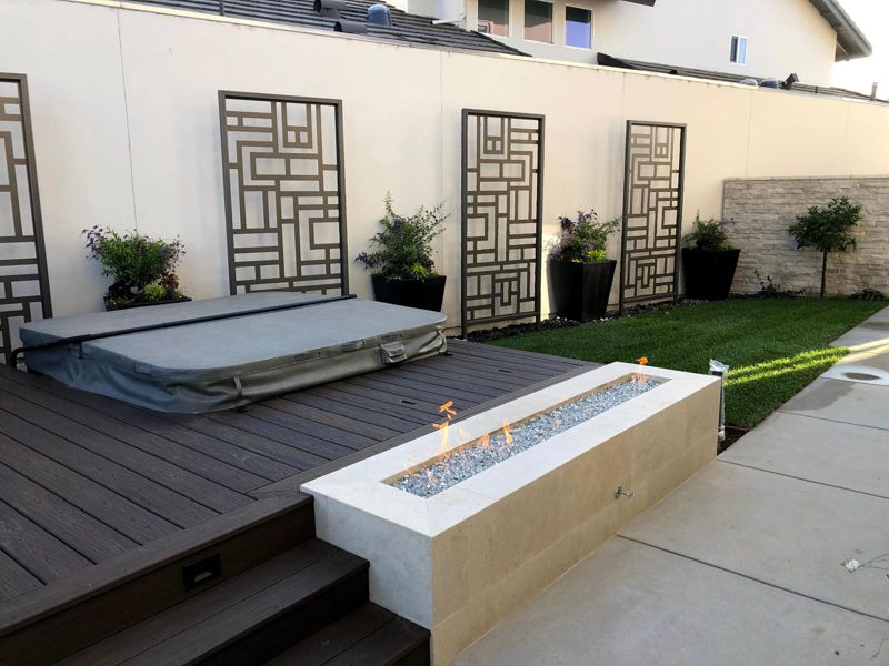 Composite deck with a lit linear stone fire pit beside a covered spa