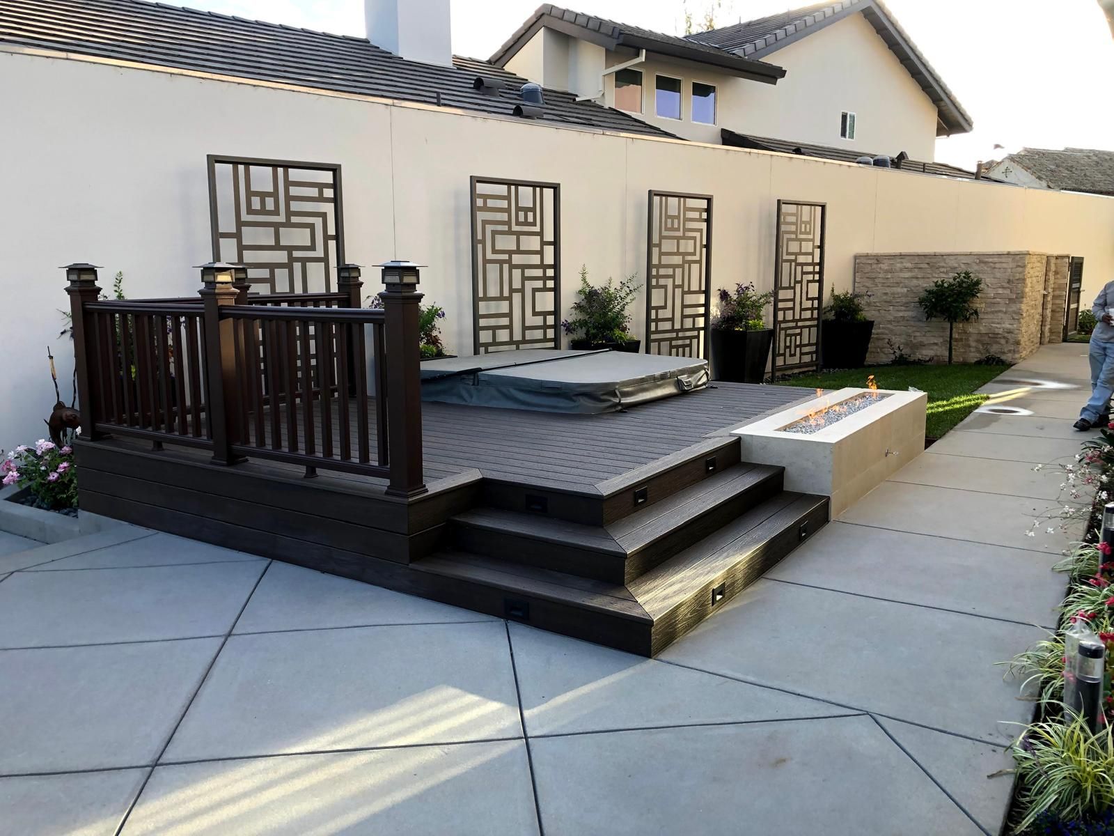 Raised composite deck with a lit linear fire pit, metal wall screens and a lawn strip