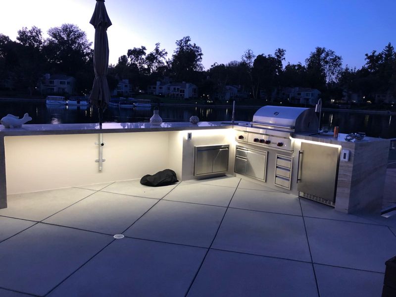 Finished L-shaped outdoor kitchen at twilight on a diagonal-scored concrete patio