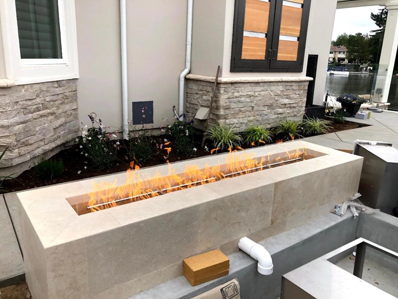 Linear travertine fire pit test-fired against a stacked-stone base, with new planting behind